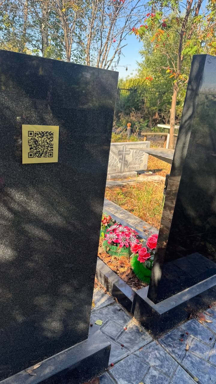 Золотистая табличка с QR‑кодом на деревянном кресте с флагами